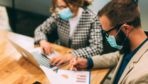 coworkers in face masks reviewing data