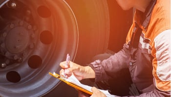 Trucker checking tire pressure with clipboard